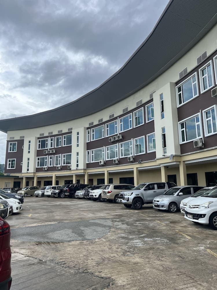 A modern multi-story building with parked cars under a cloudy sky offers a functional urban setting ideal for business travelers seeking accommodation or office space.