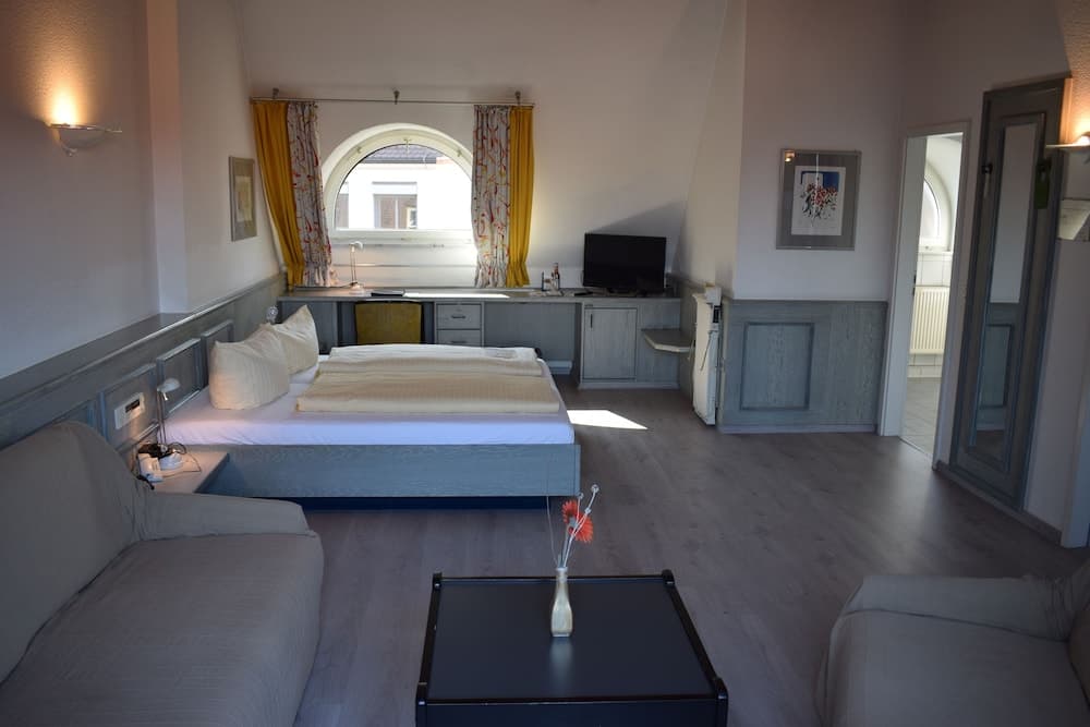 A cozy hotel room with a neatly made bed, wooden floors, and an arched window draped in yellow curtains offers a serene retreat for travelers seeking comfort and relaxation.