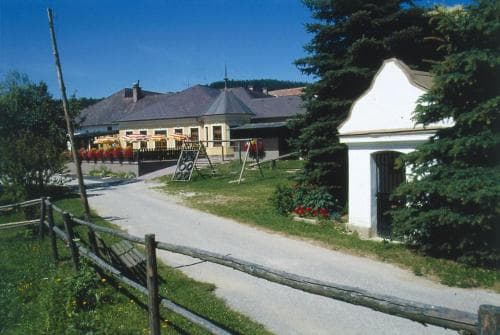 A serene rural scene featuring quaint buildings with red flowers, a wooden fence, lush greenery, and a clear blue sky, ideal for a peaceful countryside getaway.