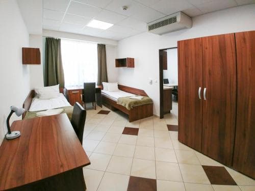 A cozy dormitory room features twin beds, wooden furniture, and a tiled floor, creating a functional and welcoming atmosphere ideal for budget travelers seeking comfortable accommodations.
