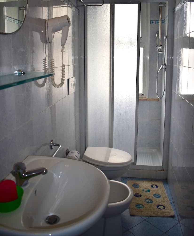 A cozy hotel bathroom features a sleek sink, wall-mounted hairdryer, frosted glass shower door, and a patterned rug, ideal for travelers seeking comfort and convenience.