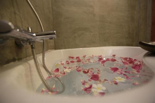 A serene bathroom scene features a bathtub filled with water and floating rose petals, creating a tranquil spa-like atmosphere ideal for relaxation and wellness retreats.