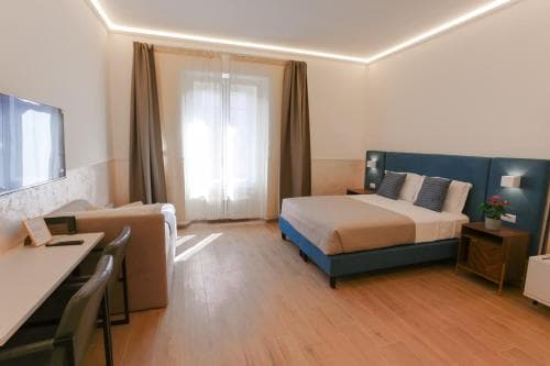 A cozy hotel room with modern decor, featuring a neatly made bed, wooden flooring, a desk area, and soft lighting, ideal for travelers seeking comfort and relaxation during their stay.