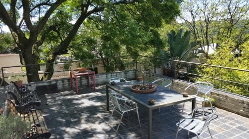 A serene rooftop patio shaded by lush trees features a metal dining set, potted plants, and cozy seating, ideal for travelers seeking a tranquil outdoor retreat.