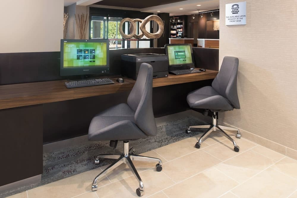 A modern hotel business center features two ergonomic chairs at a sleek desk equipped with computers and a printer, offering travelers a professional workspace in a calm and inviting atmosphere.