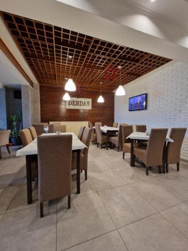 A cozy restaurant interior features modern wooden ceiling panels, warm lighting, neatly arranged tables and chairs, and a welcoming ambiance ideal for travelers seeking a comfortable dining experience.