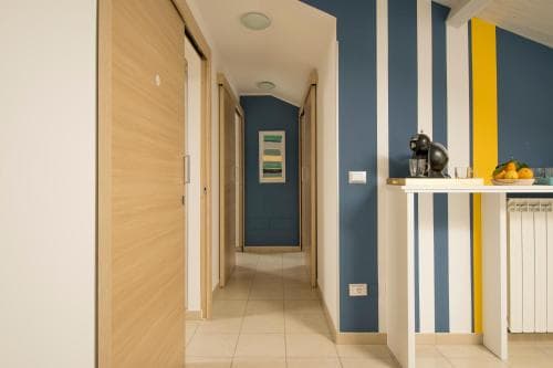 A cozy apartment hallway features vibrant blue and yellow striped walls, wooden doors, and a small table with a coffee maker and fruit, ideal for travelers seeking a stylish and welcoming accommodation.