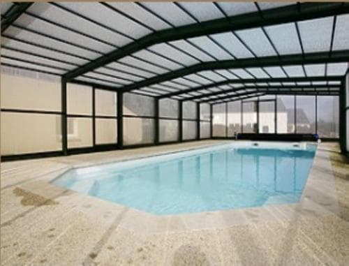 A serene indoor pool surrounded by large glass windows under a modern arched roof, ideal for travelers seeking relaxation in a private, all-weather setting.