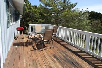 A serene outdoor deck with wooden flooring, white railings, and patio furniture offers a cozy spot for relaxation amidst lush greenery, ideal for travelers seeking a peaceful retreat.