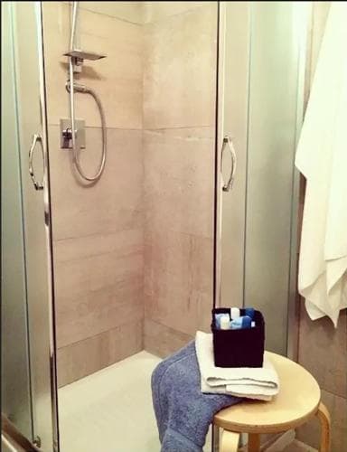A serene hotel bathroom features a modern glass-enclosed shower with beige tiles, a wooden stool holding neatly folded towels and toiletries, ideal for travelers seeking comfort and cleanliness.