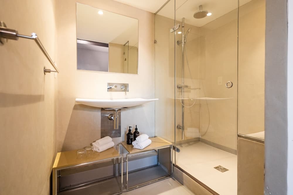 A modern bathroom with a sleek glass-enclosed shower, minimalist sink, neatly folded towels, and ambient lighting creates a serene and luxurious atmosphere ideal for travelers seeking comfort and style in their accommodations.