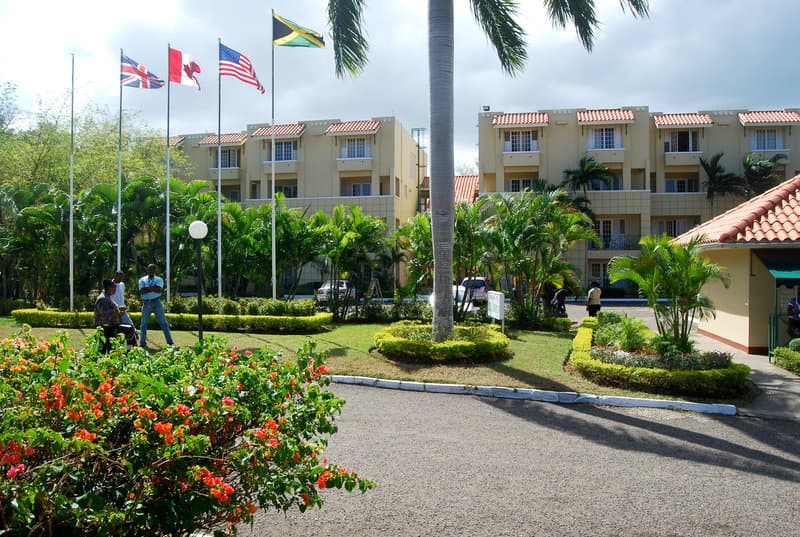 A vibrant tropical resort entrance features lush greenery, colorful flowers, international flags, and palm trees, creating an inviting atmosphere ideal for vacationers seeking relaxation and cultural immersion.