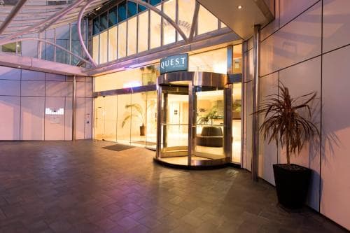 A modern hotel entrance featuring a revolving glass door illuminated by warm lighting, surrounded by sleek architecture and potted plants, evokes a welcoming and upscale atmosphere ideal for travelers seeking comfort and style.