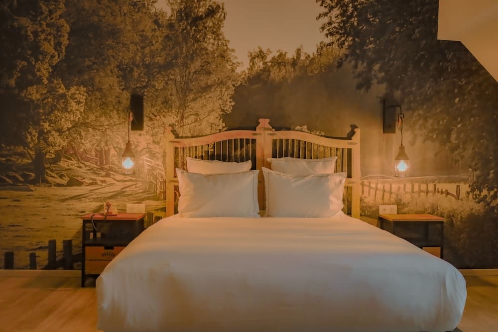 A cozy bedroom with a rustic wooden bed and warm lighting against a serene forest mural backdrop, ideal for travelers seeking relaxation in a tranquil lodge setting.