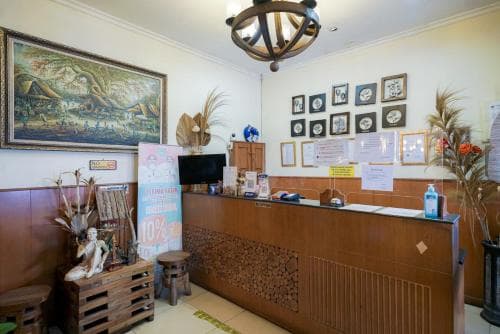 A cozy hotel reception adorned with tropical decor, framed artwork, and informational notices creates a welcoming atmosphere ideal for travelers seeking a comfortable stay.