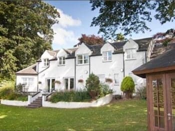 A charming white house with a well-manicured lawn and blooming flower boxes invites travelers seeking a serene countryside retreat, perfect for a relaxing getaway.