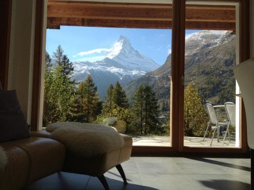A cozy indoor lounge with plush seating overlooks the majestic Matterhorn through large windows, offering travelers a serene retreat amidst alpine scenery ideal for relaxation and inspiration.