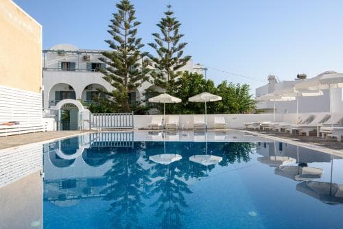 A serene hotel courtyard features a crystal-clear pool reflecting tall pine trees and white buildings under a sunny sky, ideal for travelers seeking relaxation and leisure.