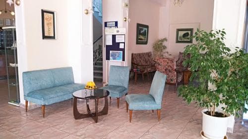 A cozy hotel lobby features teal upholstered seating around a wooden coffee table, framed artwork on the walls, and lush greenery, creating a welcoming atmosphere ideal for travelers seeking relaxation.