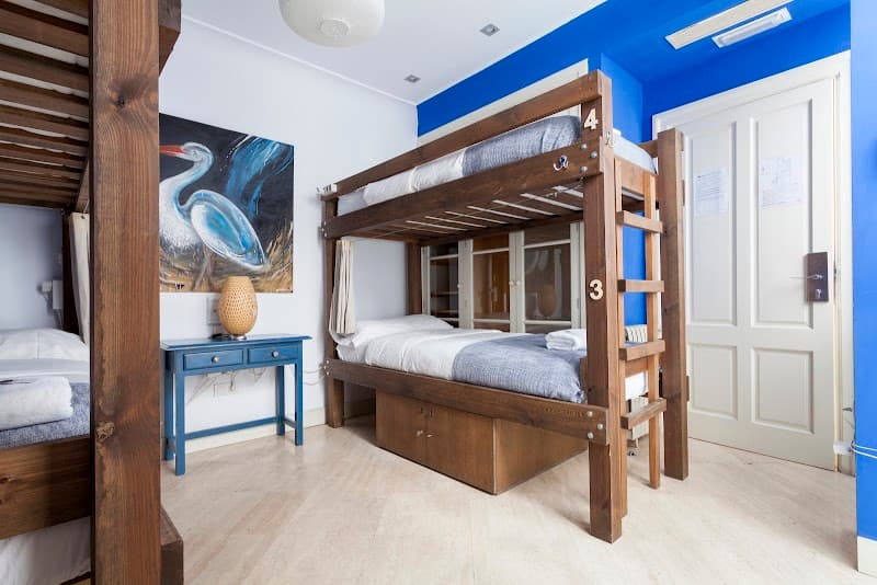 A cozy dorm room at La Banda Rooftop Hostel in Sevilla's historic Casco Antiguo features wooden bunk beds, vibrant blue walls, and artistic decor, ideal for budget travelers seeking comfort and charm.