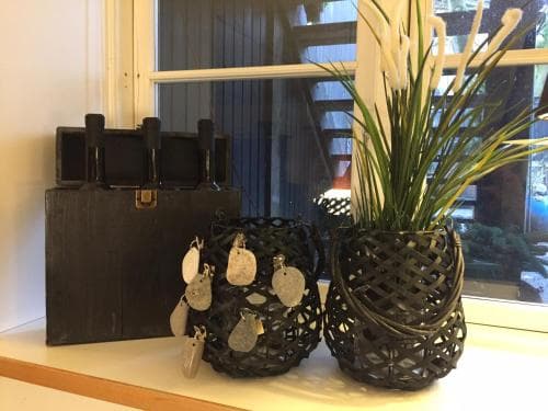 A serene indoor display features intricate black woven baskets holding decorative stones and lush green plants, set against a window backdrop, ideal for home decor enthusiasts seeking unique artisanal pieces.