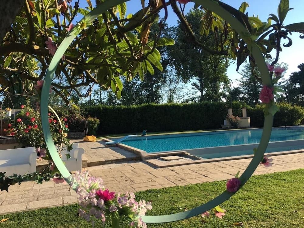 A serene garden scene framed by a floral archway showcases a tranquil pool surrounded by lush greenery, ideal for a relaxing vacation retreat.
