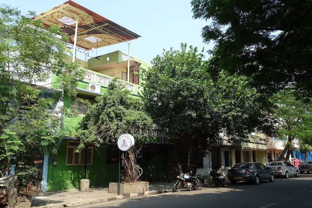 A vibrant green building with balconies and lush trees creates a serene urban street scene, ideal for travelers seeking a peaceful neighborhood ambiance with parked motorcycles and cars adding to the local charm.