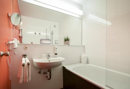 A modern hotel bathroom features a sleek sink, bathtub, and large mirror, creating a clean and inviting atmosphere ideal for travelers seeking comfort and convenience.