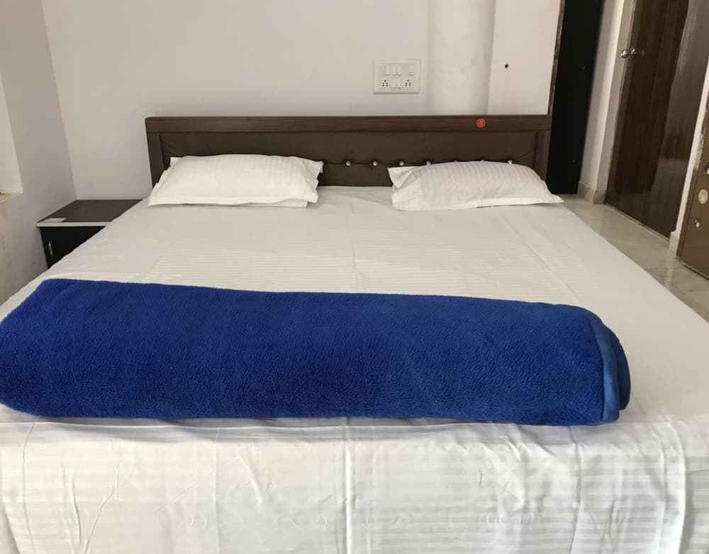 A cozy hotel room features a neatly made bed with white linens and a blue blanket, set against a minimalist backdrop with a wooden headboard, ideal for travelers seeking comfort and simplicity.