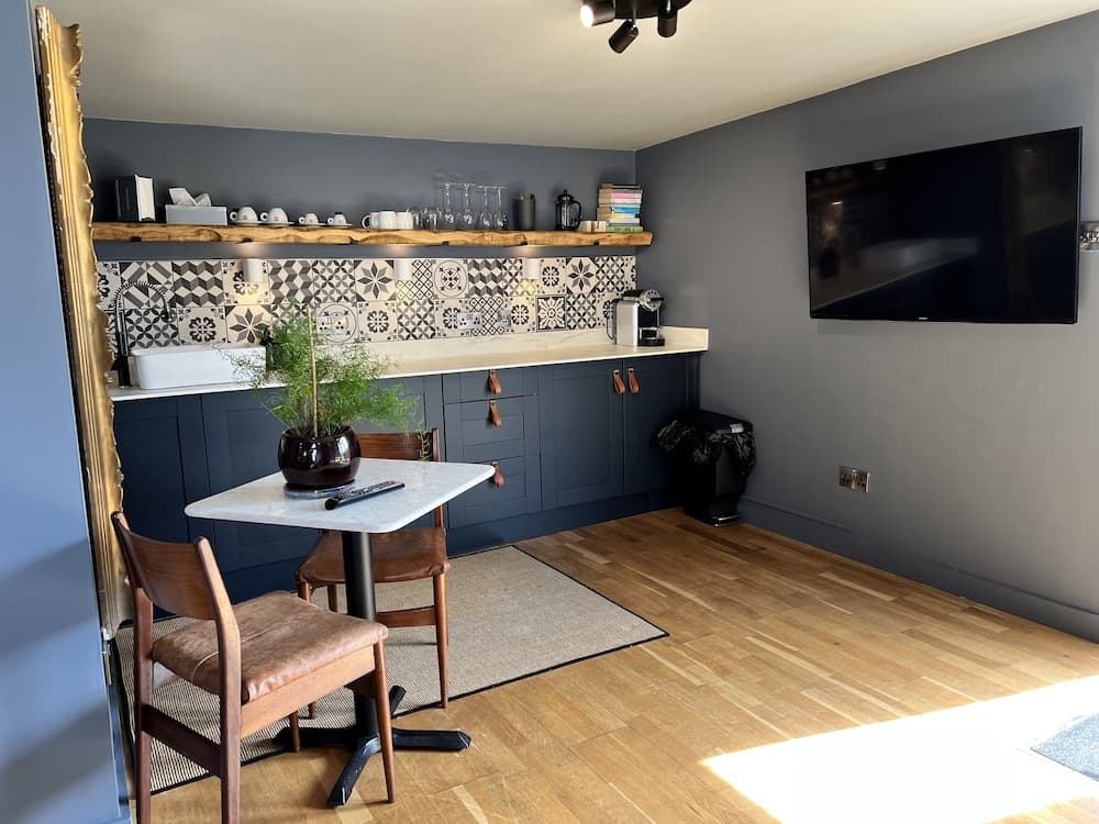 A cozy modern kitchenette with dark blue cabinets, patterned tiles, and a small dining area featuring wooden chairs and a marble table, perfect for a comfortable stay in a boutique hotel or vacation rental.