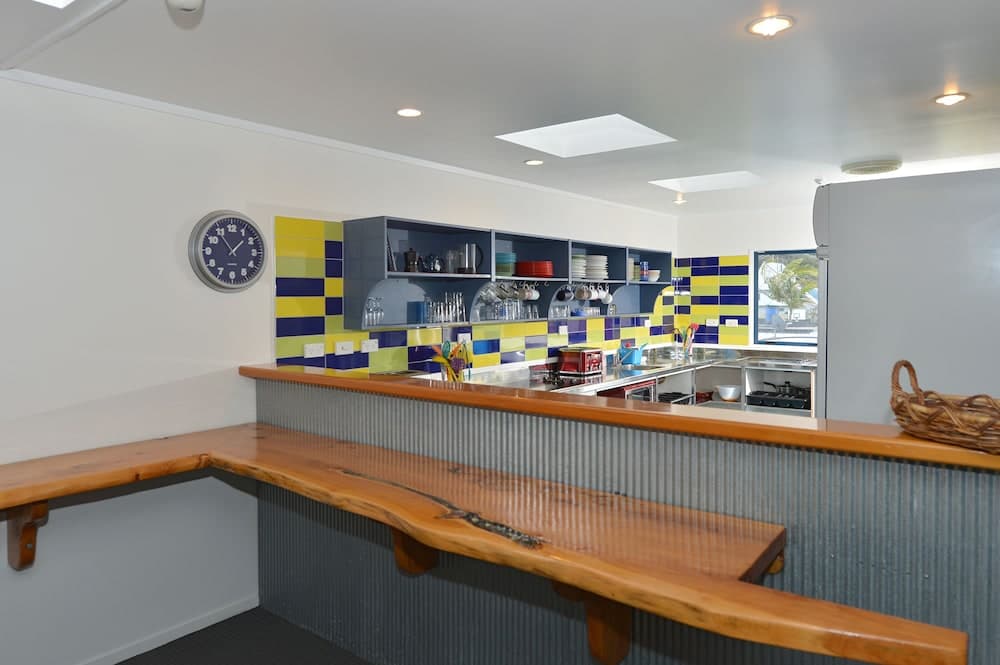 A cozy communal kitchen with vibrant blue and yellow tiled walls, wooden benches, and ample shelving creates an inviting atmosphere ideal for group accommodations or shared living spaces.