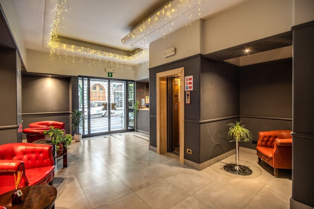 A cozy hotel lobby features vibrant red leather chairs, twinkling string lights, and a modern elevator, creating an inviting atmosphere ideal for travelers seeking comfort and style.