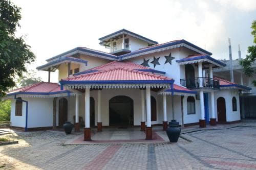 A serene courtyard features a traditional white building with red-tiled roofs and blue accents, surrounded by lush greenery, ideal for cultural exploration and heritage tourism.