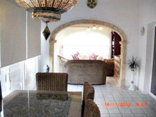 A cozy indoor dining area with wicker furniture, ornate chandeliers, and an arched doorway leading to a warmly lit living space evokes a serene and inviting atmosphere, perfect for travelers seeking a charming and comfortable accommodation experience.