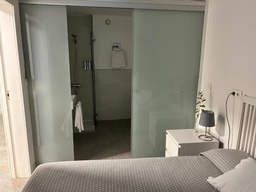 A cozy bedroom with a neatly made bed and frosted glass doors leading to an adjacent bathroom creates a serene and modern atmosphere, ideal for travelers seeking comfort and privacy in a compact space.