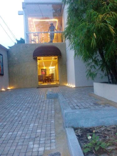 A cozy evening scene at a modern house with warm interior lighting, a tiled patio, lush bamboo plants, and inviting outdoor seating, perfect for travelers seeking a tranquil retreat.