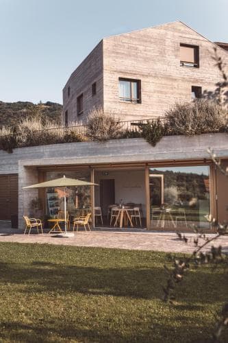 A serene modern wooden house with a rooftop garden overlooks a cozy outdoor seating area with tables, chairs, and an umbrella, ideal for travelers seeking a tranquil retreat in a scenic countryside setting.