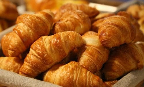 A basket brimming with golden, flaky croissants evokes a cozy bakery atmosphere, perfect for travelers seeking a delightful continental breakfast experience.