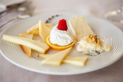 A beautifully arranged cheese plate featuring assorted cheeses, a dollop of whipped cream topped with a raspberry, and garnished with nuts, perfect for a gourmet dining experience or a culinary travel blog.