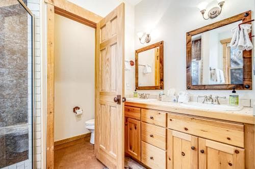 A cozy bathroom with wooden cabinetry, dual sinks, and a walk-in shower offers a rustic charm ideal for travelers seeking a warm and inviting retreat.