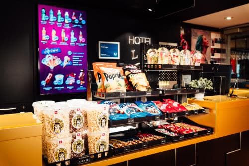 A cozy hotel lobby snack bar features vibrant displays of popcorn, candy, and snacks under warm lighting, creating an inviting atmosphere perfect for travelers seeking quick refreshments.