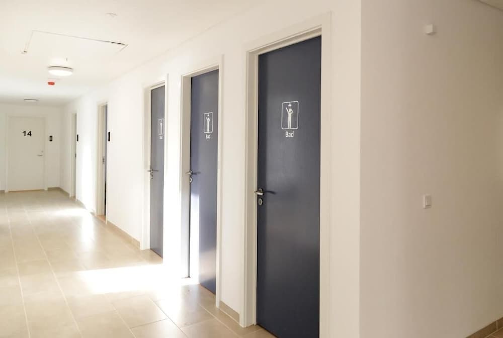 A clean, modern hotel corridor with tiled floors, white walls, and blue doors marked "Bad" offers a serene atmosphere ideal for travelers seeking a quiet stay.