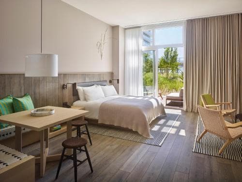 A cozy hotel room with wooden floors, modern furnishings, and large windows overlooking greenery, exudes a serene and inviting atmosphere ideal for travelers seeking relaxation and comfort.