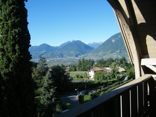 A serene balcony view captures lush green valleys and majestic mountains under a clear blue sky, ideal for travelers seeking tranquil retreats in scenic alpine regions.