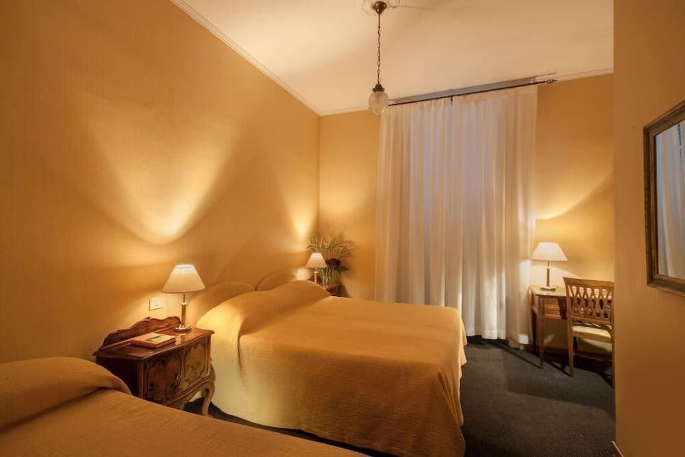 A cozy hotel room with warm lighting, beige walls, two neatly made beds, wooden furniture, and a serene ambiance is ideal for travelers seeking comfort and relaxation.