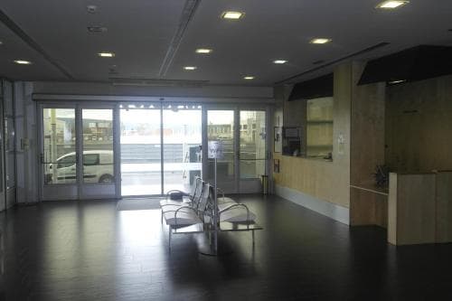 A modern, minimalist waiting area with sleek chairs and large glass doors leading to an outdoor view, ideal for travelers seeking a quiet space in a transportation hub or office building.