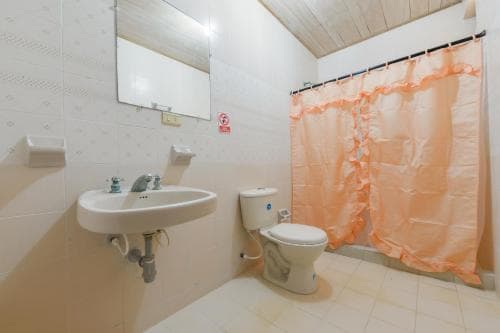 A cozy bathroom with white tiled walls, a sink, toilet, and peach-colored shower curtain creates a clean and inviting atmosphere, ideal for travelers seeking comfort in accommodations.