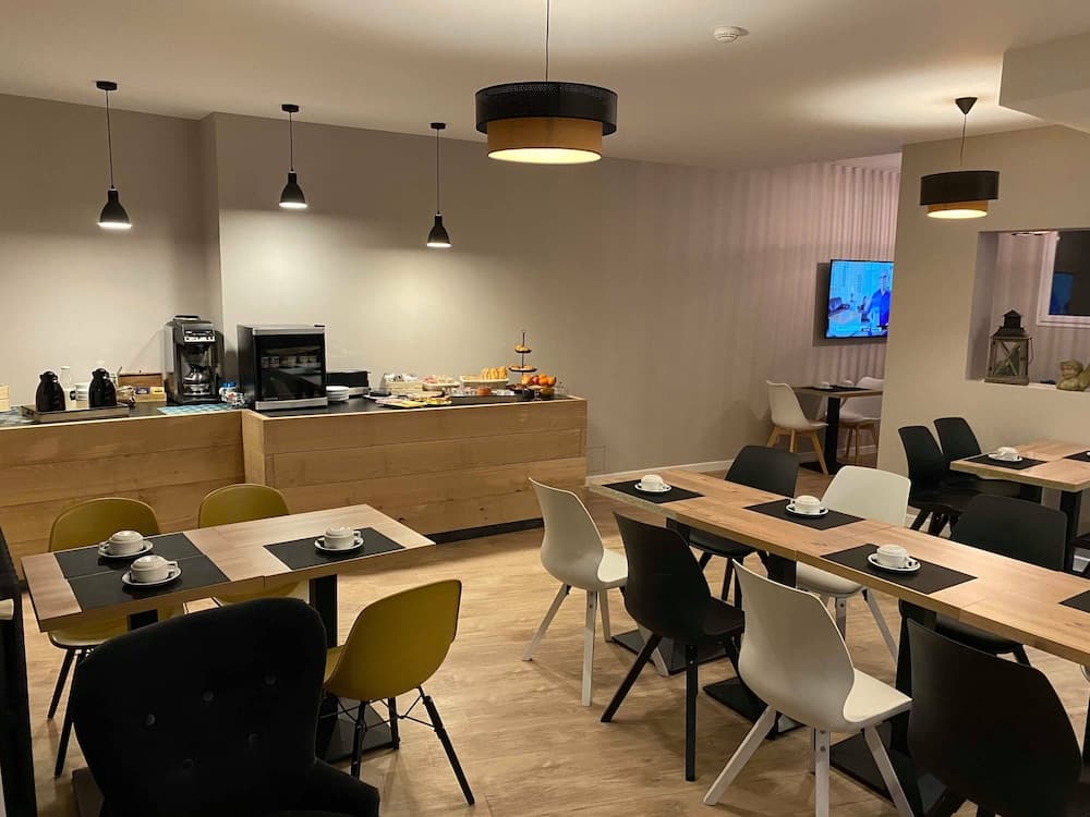 A cozy café with wooden tables, colorful chairs, and modern pendant lights offers a welcoming atmosphere for travelers seeking a quiet spot to enjoy breakfast or coffee.