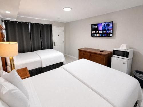 A cozy hotel room features two neatly made beds, a mounted TV displaying vibrant content, and essential amenities like a microwave and dresser, ideal for travelers seeking comfort and convenience.
