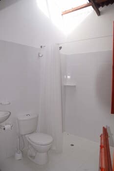 A bright, minimalist bathroom with white tiles, a skylight, and simple fixtures creates a clean and serene atmosphere, ideal for travelers seeking a peaceful accommodation space.
